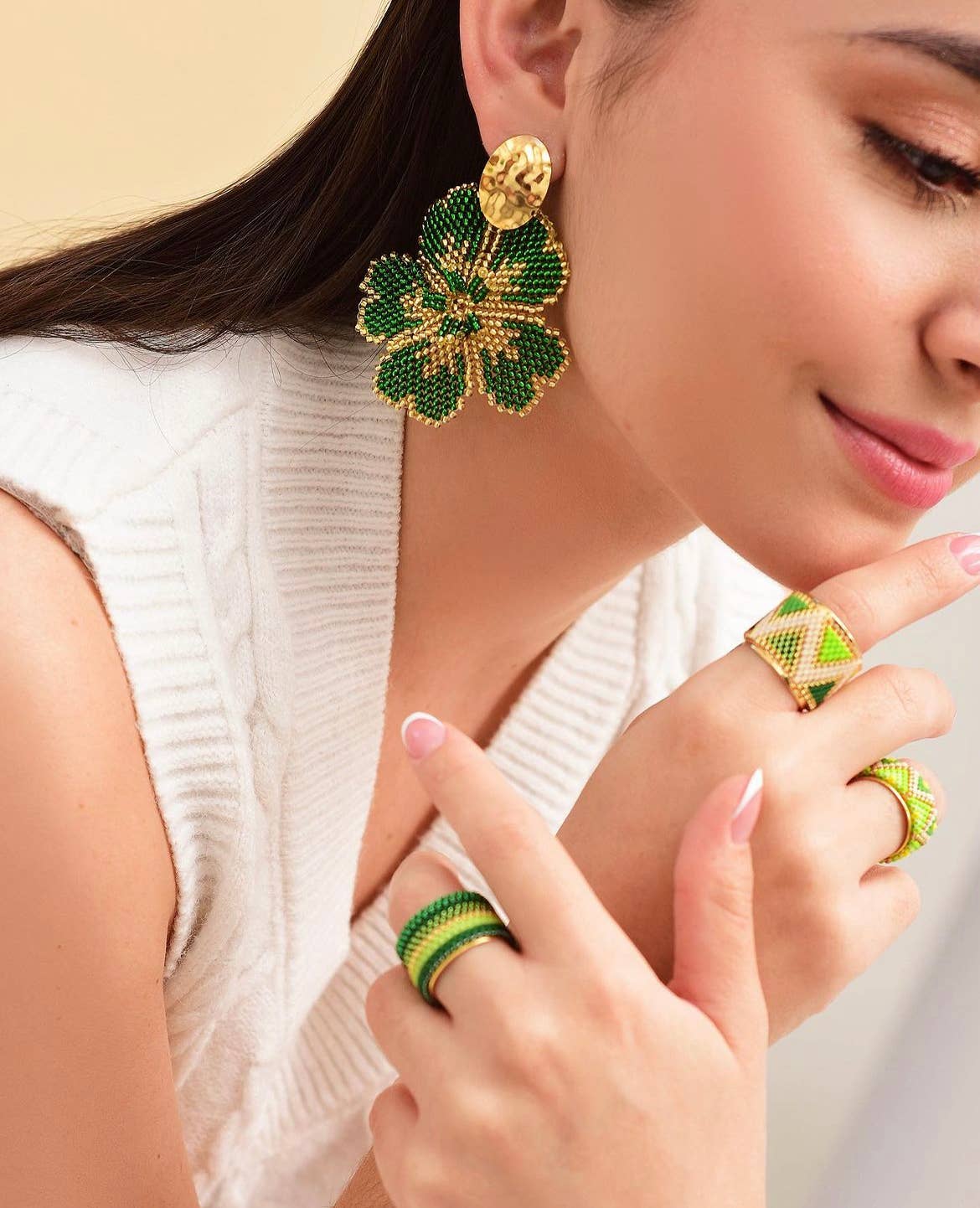 Woman wearing green and gold floral earrings and rings on a neutral background
