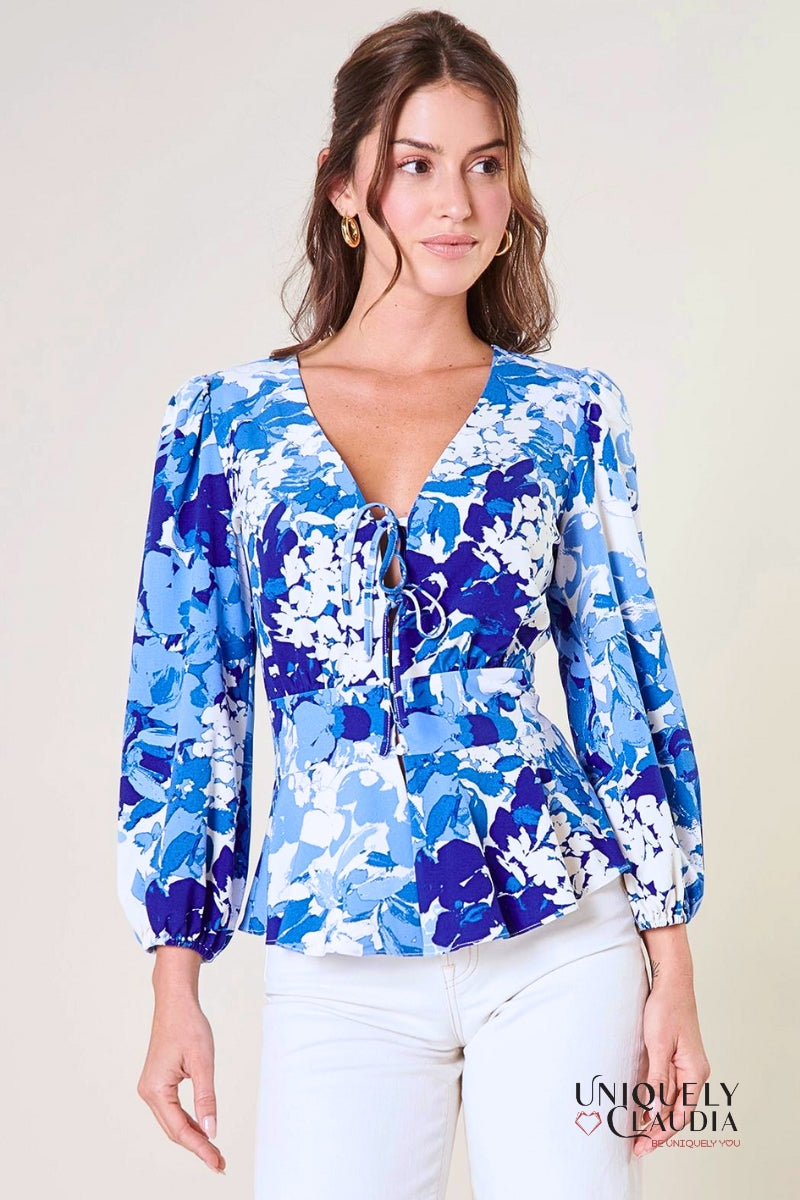 A woman modeling a blue peplum top with long balloon sleeves, a deep v-neckline with tie details, and a flouncy ruffle waist.