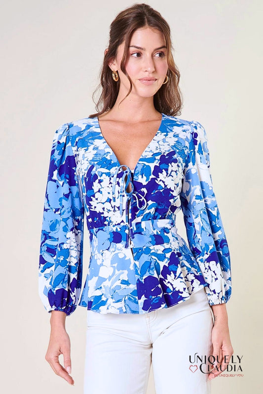 A woman modeling a blue peplum top with long balloon sleeves, a deep v-neckline with tie details, and a flouncy ruffle waist.