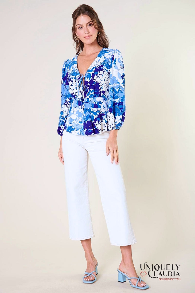 A woman modeling a blue peplum top with long balloon sleeves, a deep v-neckline with tie details, and a flouncy ruffle waist.