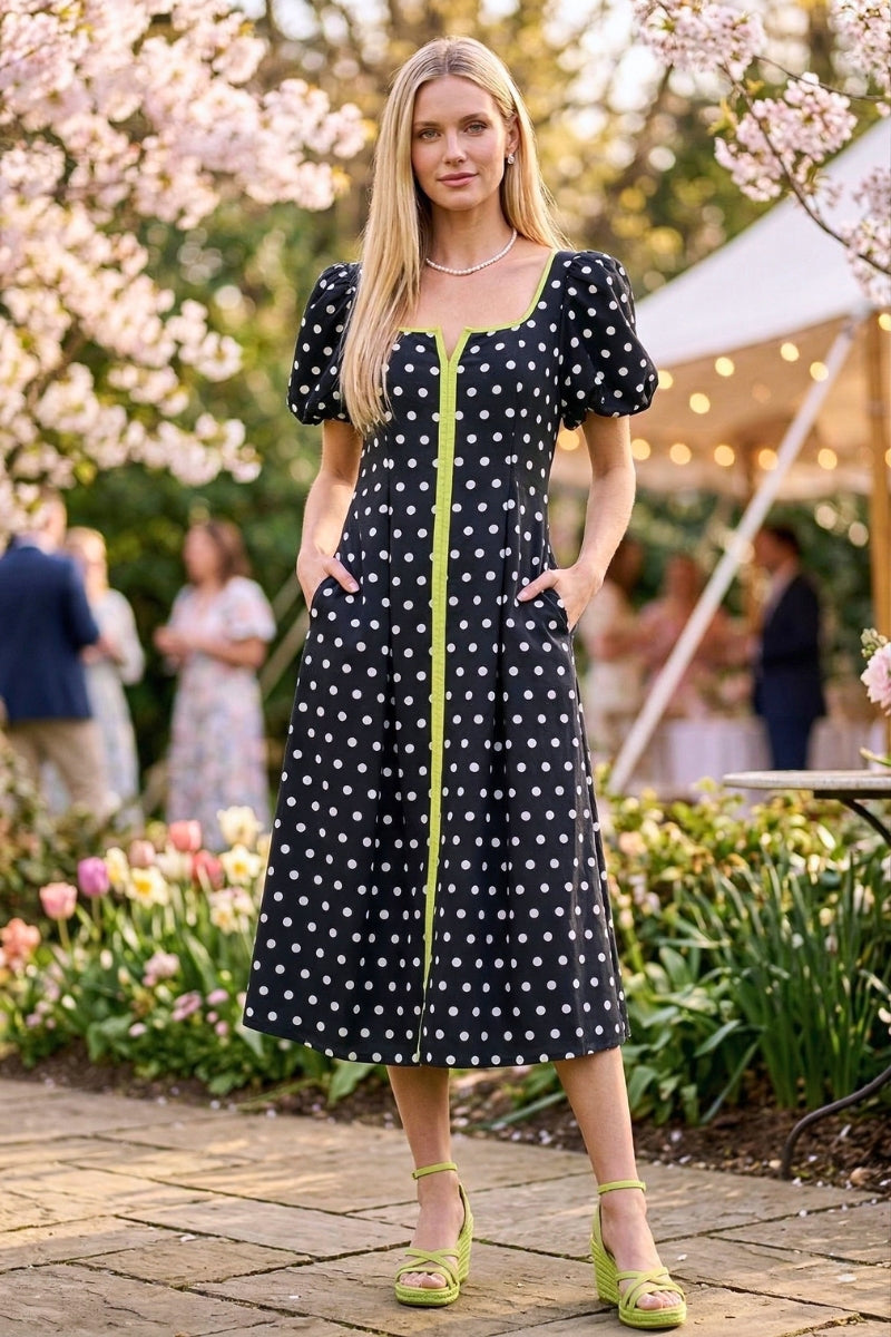 Woman in a polka dot dress standing outdoors with cherry blossoms and people in the background