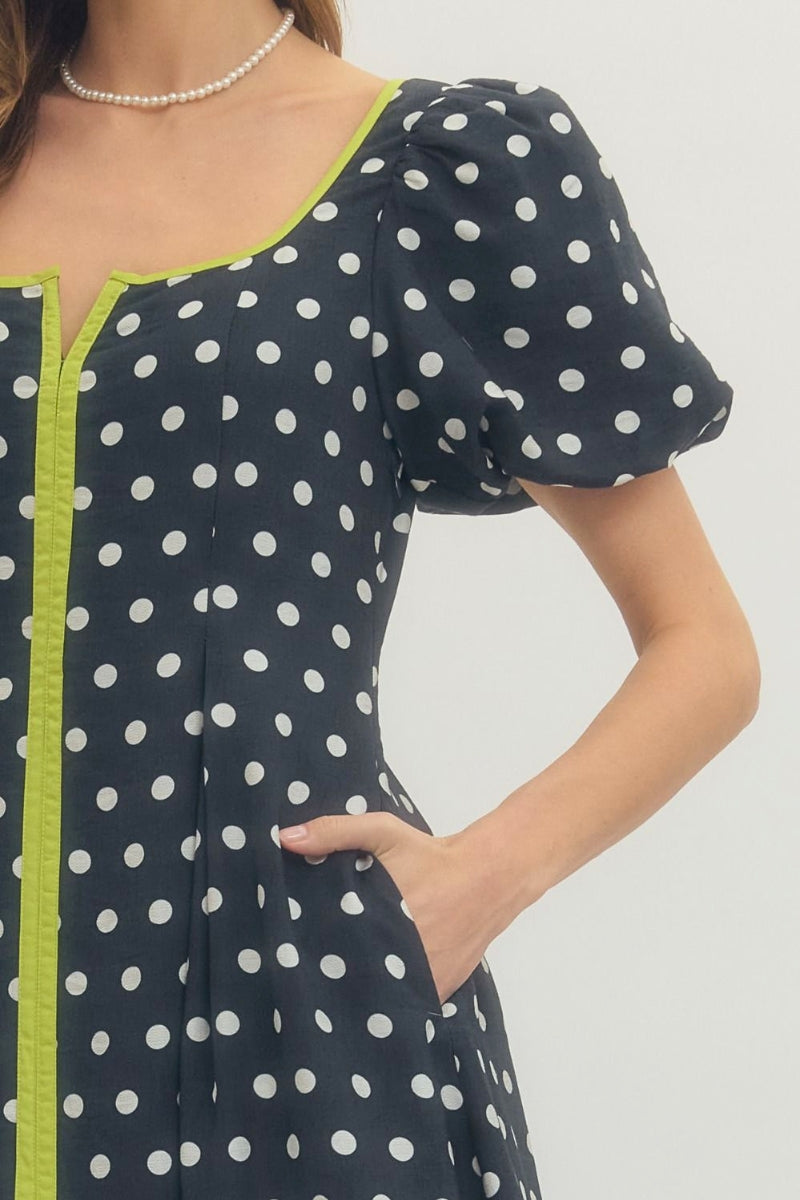 Woman wearing a polka dot dress with green trim on a plain background