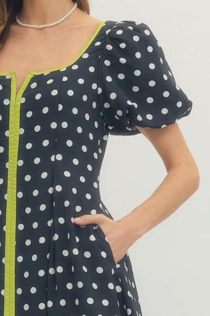 Woman wearing a polka dot dress with green trim on a plain background
