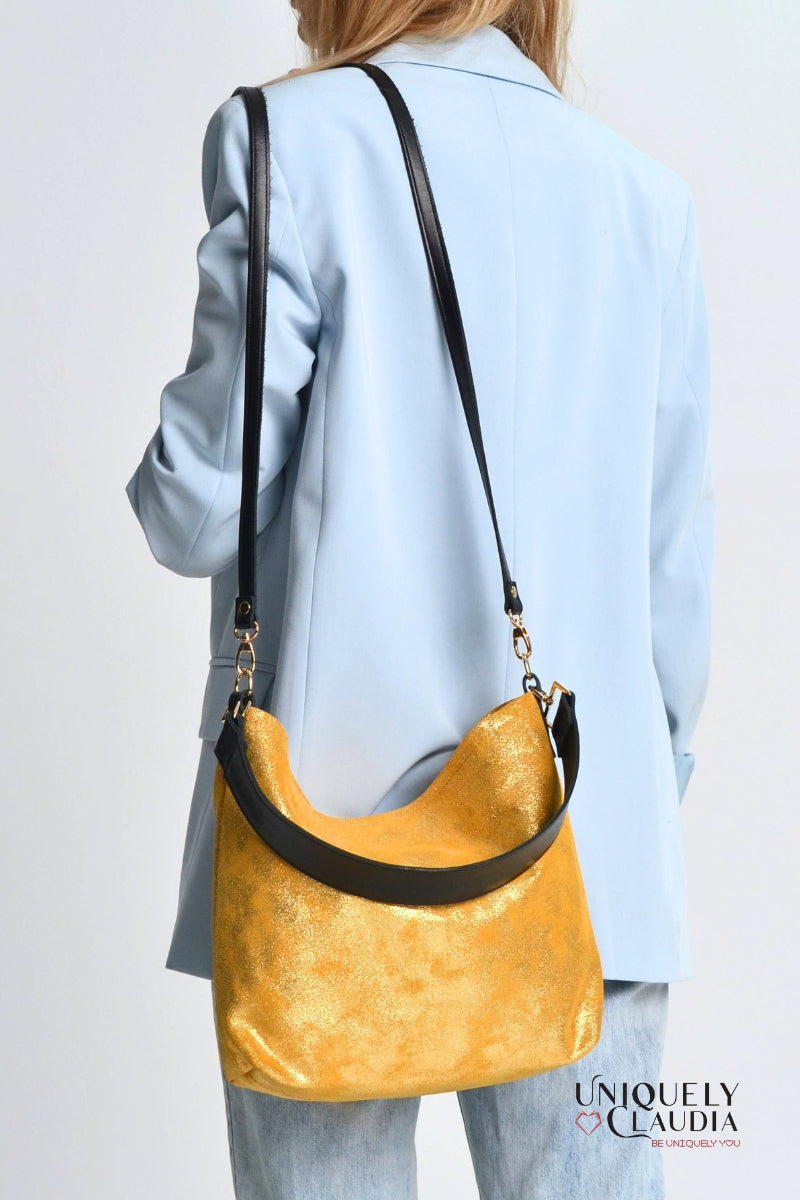 Woman wearing a light blue coat with a gold handbag over one shoulder on a plain background.