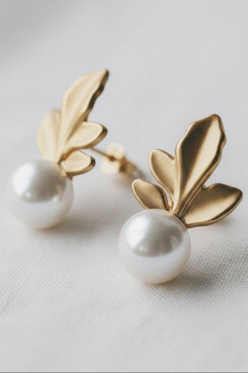Gold leaf earrings with pearl centers on a light background