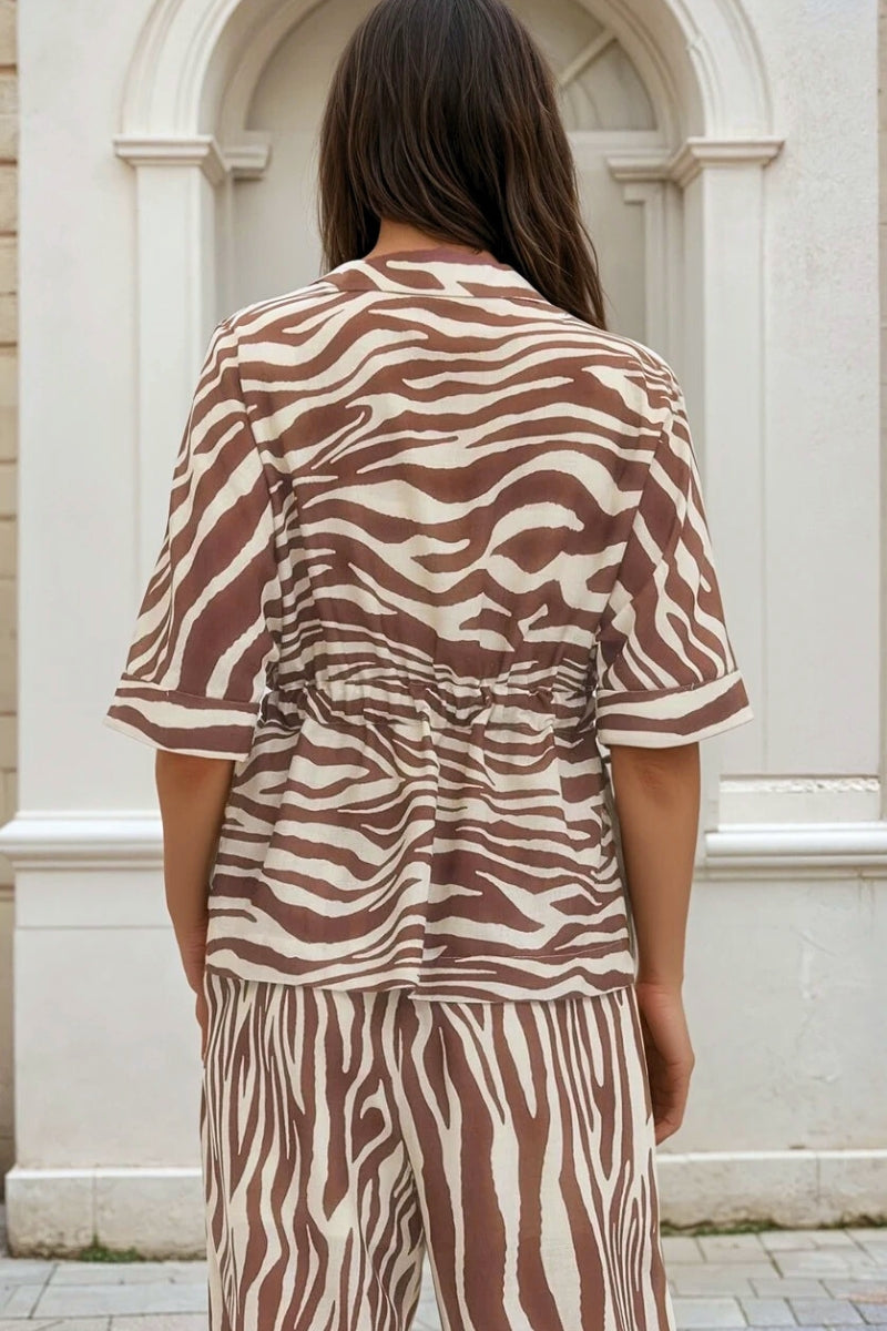 Person wearing a brown and white zebra print outfit in front of a white building.