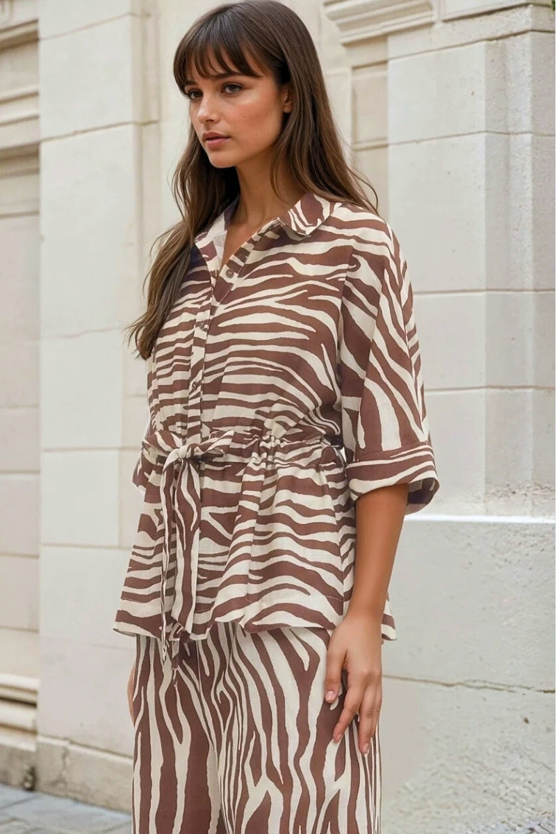 Woman wearing a zebra print outfit standing against a light-colored wall.