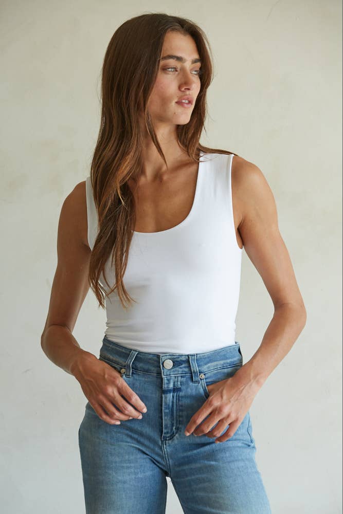 Woman wearing a white tank top and blue jeans against a plain background
