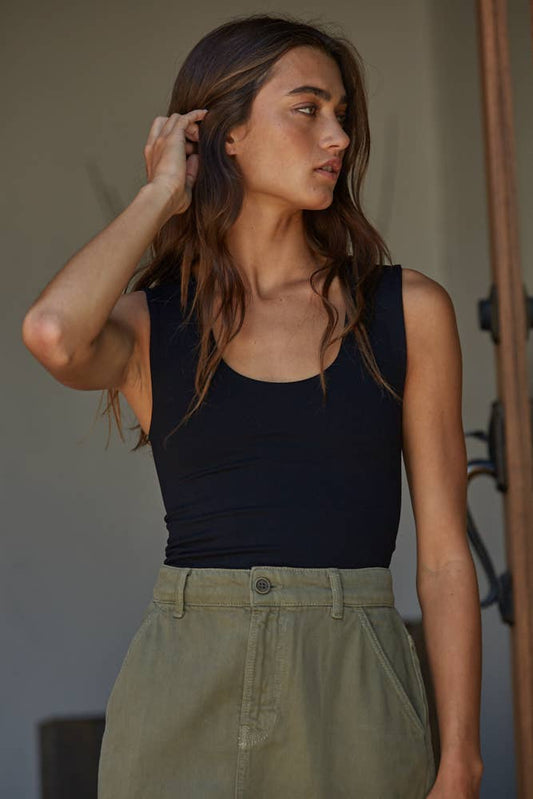 Woman wearing a black sleeveless top and green pants indoors.