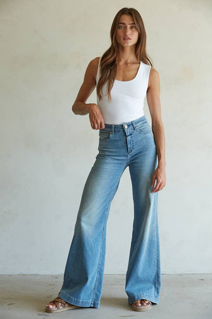 Woman wearing a white tank top and blue jeans against a plain background