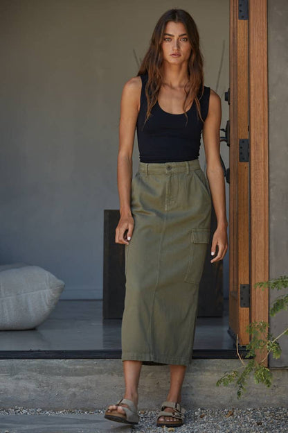 Woman wearing a black tank top and green skirt standing in a doorway.