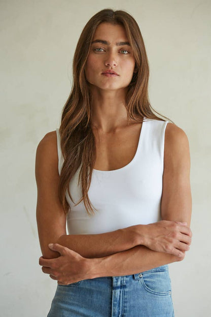 Woman wearing a white tank top and blue jeans against a plain background