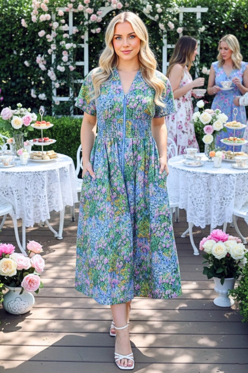 Woman in a floral dress standing outdoors with tables and flowers in the background