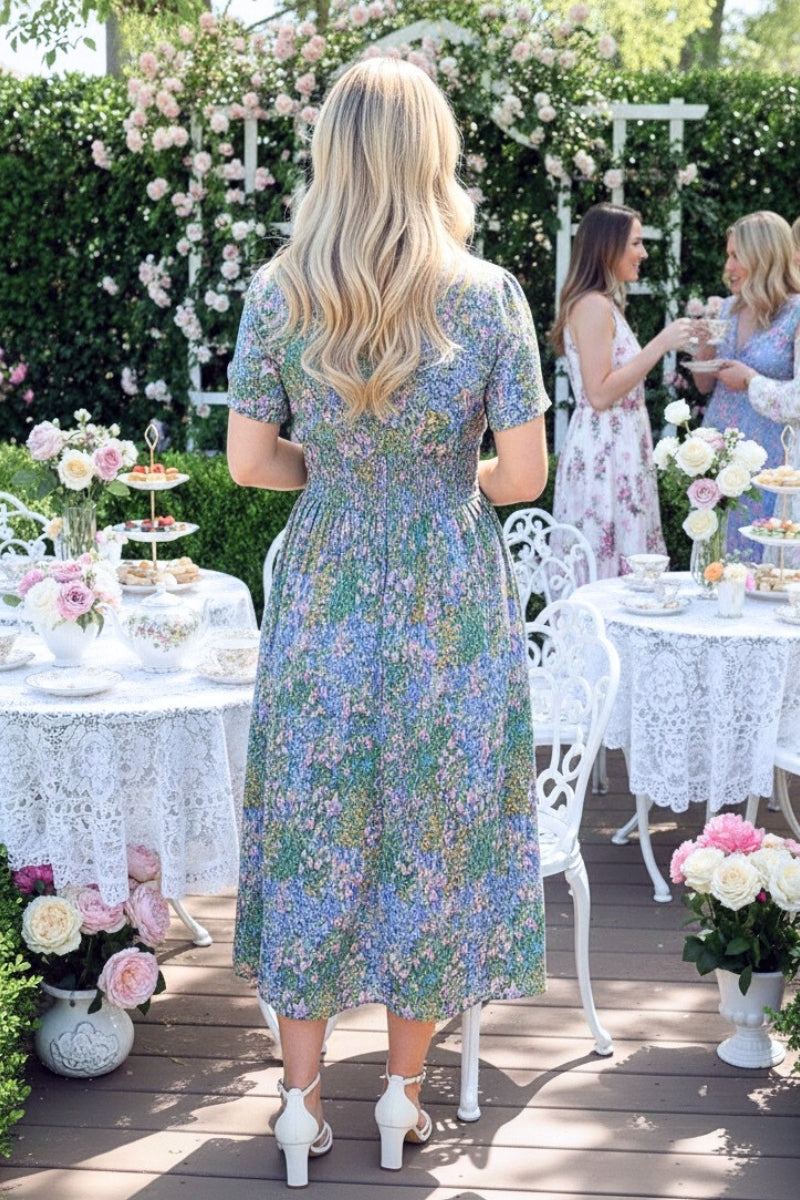 Woman in a floral dress standing at an outdoor event with tables and floral decorations.