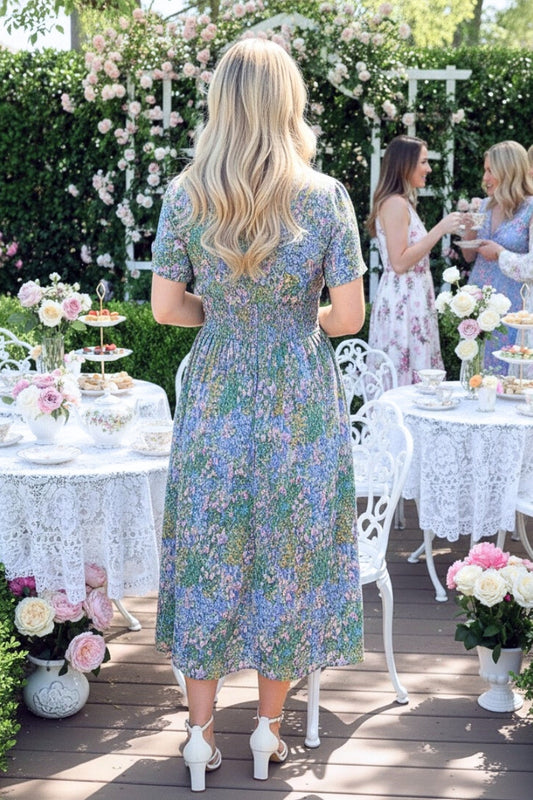 Woman in a floral dress standing at an outdoor event with tables and floral decorations.