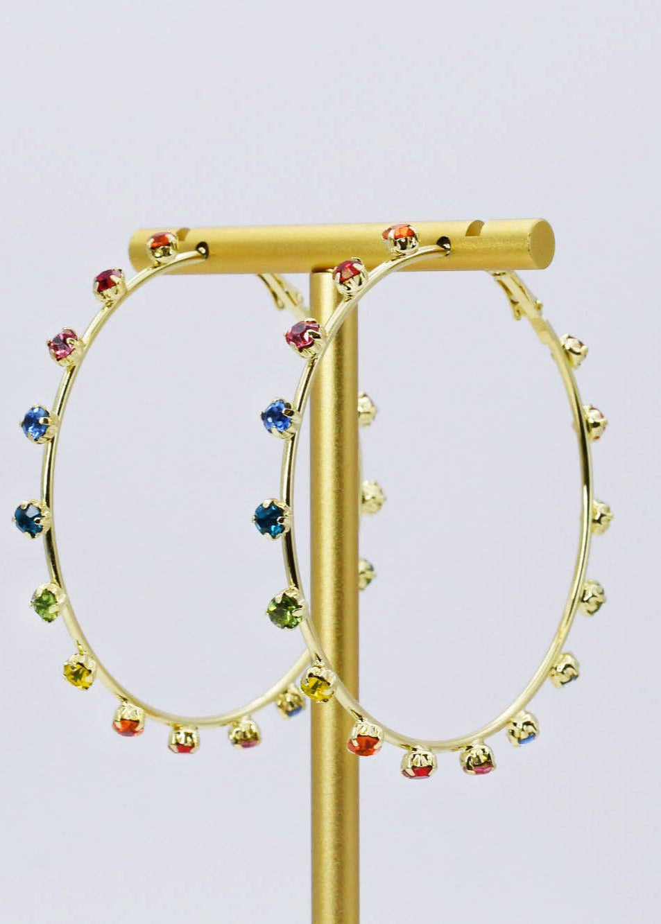 Gold hoop earrings with colorful beads on a gold stand against a light purple background