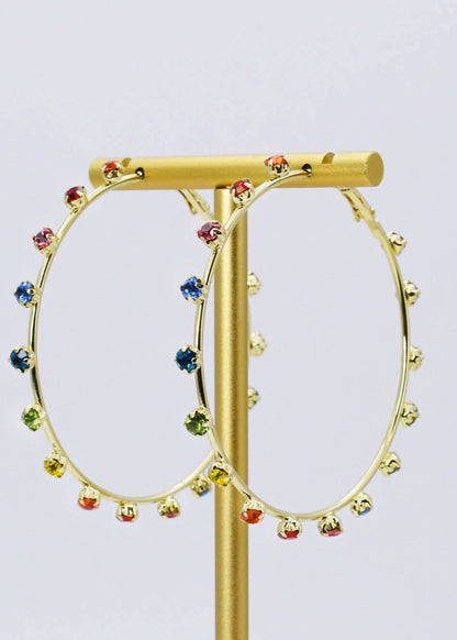 Gold hoop earrings with colorful beads on a gold stand against a light purple background