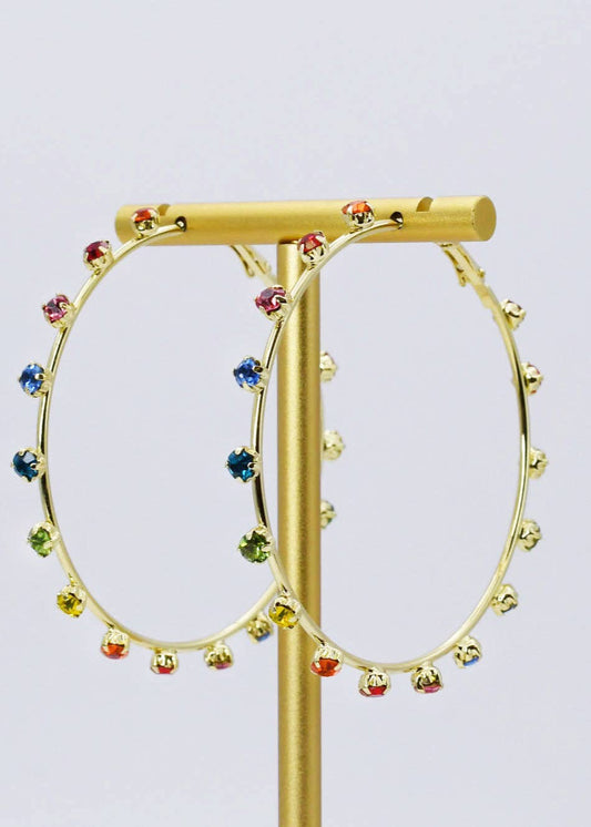 Gold hoop earrings with colorful beads on a gold stand against a light purple background