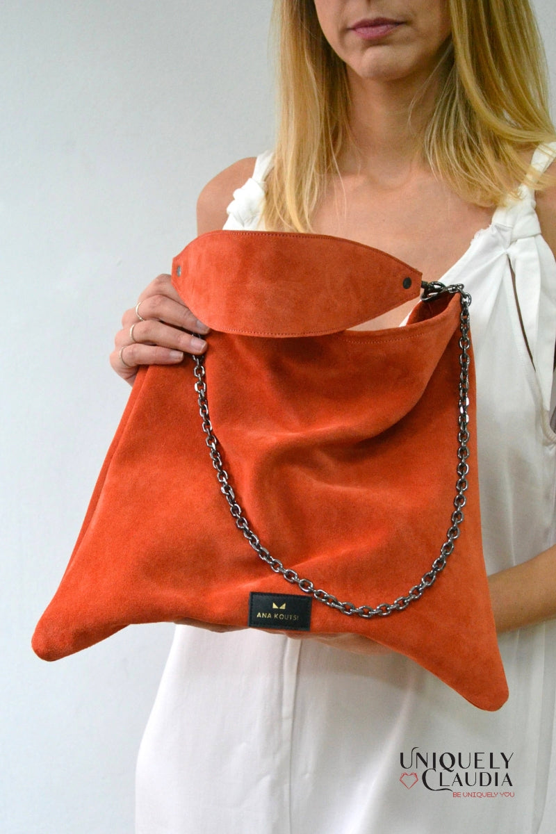 Orange suede handbag with chain detail held by a person against a white background