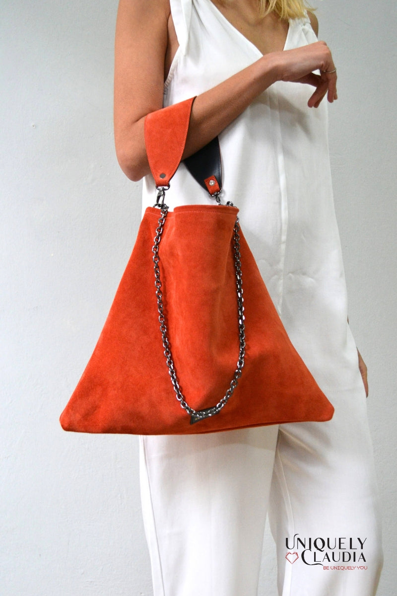 Orange handbag with chain detail held by a person wearing a white outfit, brand 'Uniquely Claudia' visible.