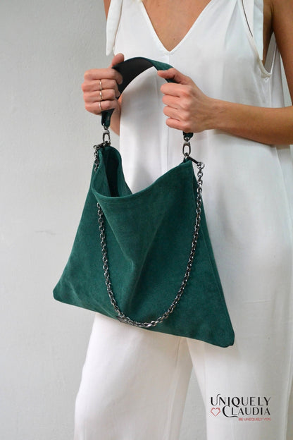 Green handbag with chain detail held by a person wearing a white outfit, against a plain background.