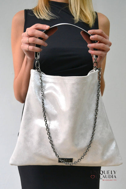 Person holding a silver handbag with a chain detail against a plain background