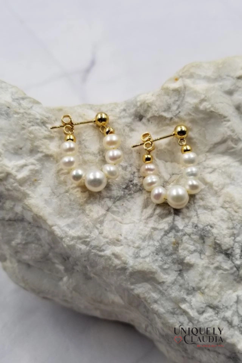 Pearl hoop earrings with gold accents on a textured stone surface, branded 'Uniquely Claudia'.