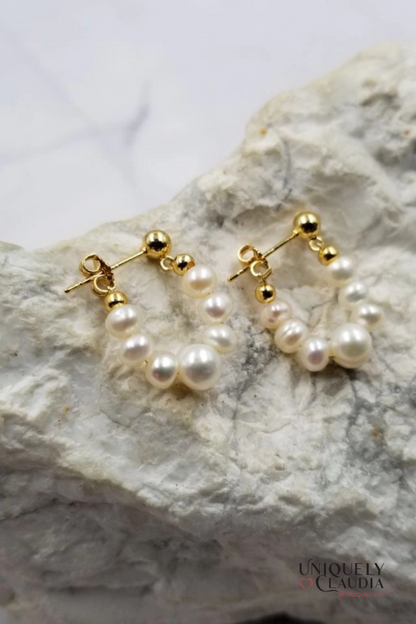 Pearl hoop earrings with gold posts on a textured white surface