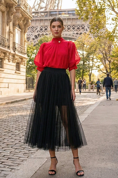 Woman in a red blouse and black tulle skirt standing in front of the Eiffel Tower.