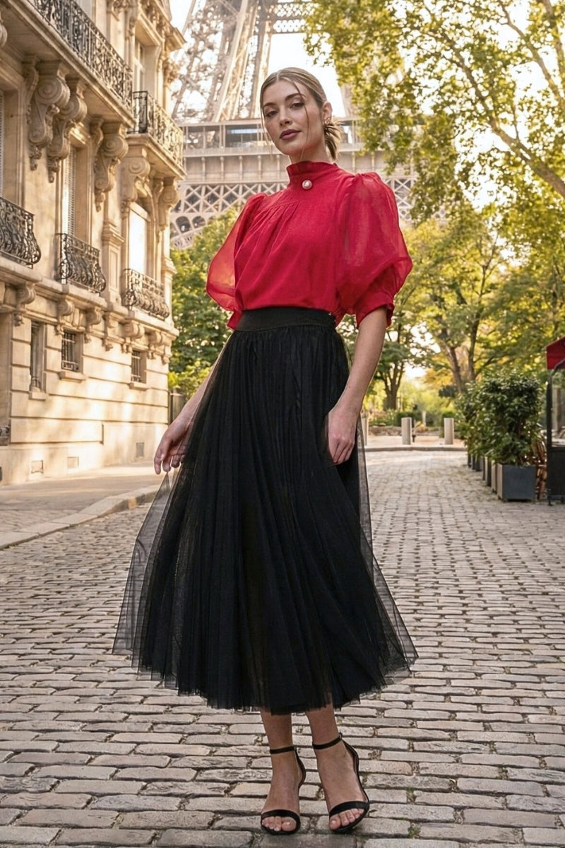 Woman in a red blouse and black skirt standing on a street with the Eiffel Tower in the background.