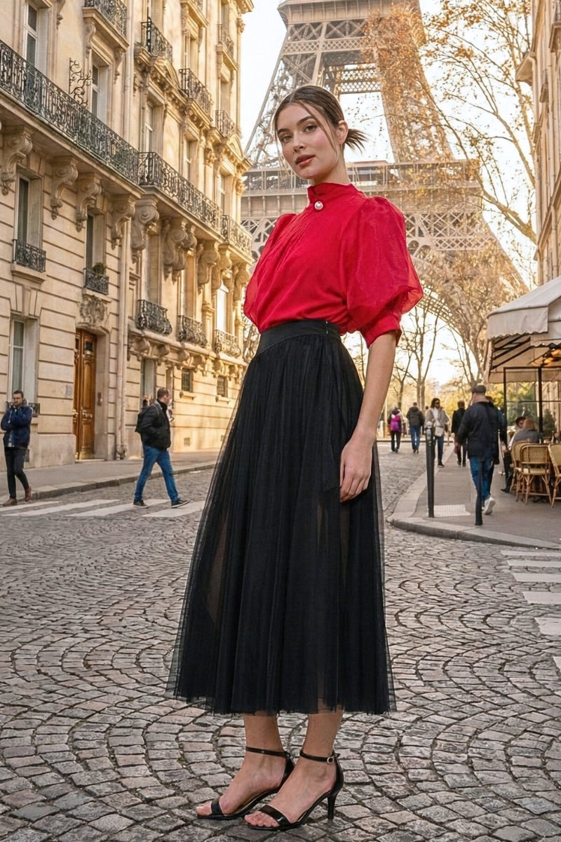 Woman in a red blouse and black skirt standing in front of the Eiffel Tower.