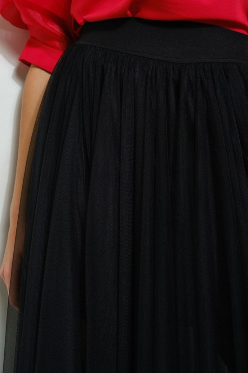 Black skirt worn by a person with a red top, against a neutral background