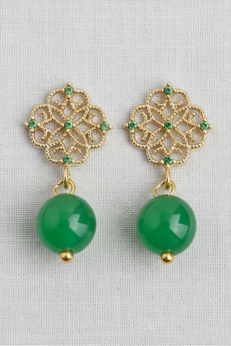 Gold earrings with green beads on a light gray background
