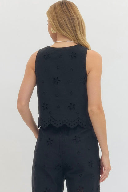 Woman wearing a black sleeveless top and pants with floral cut-out details on a white background