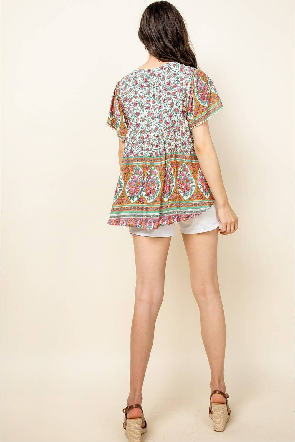 Woman wearing a colorful patterned top and white shorts on a beige background