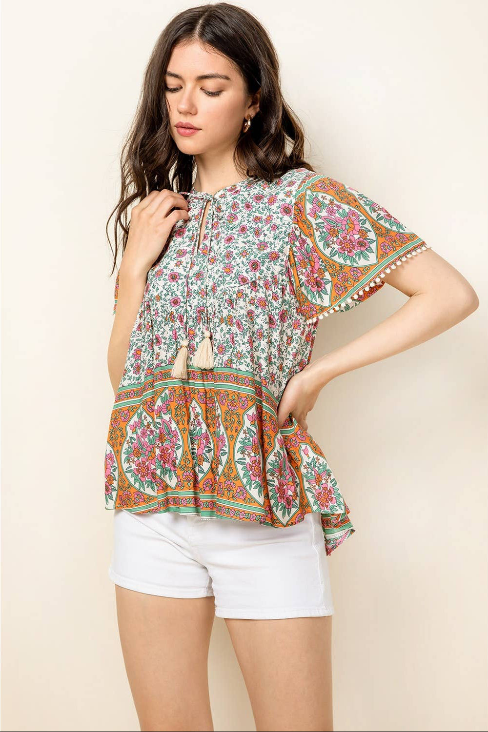 Woman wearing a patterned blouse and white shorts on a beige background