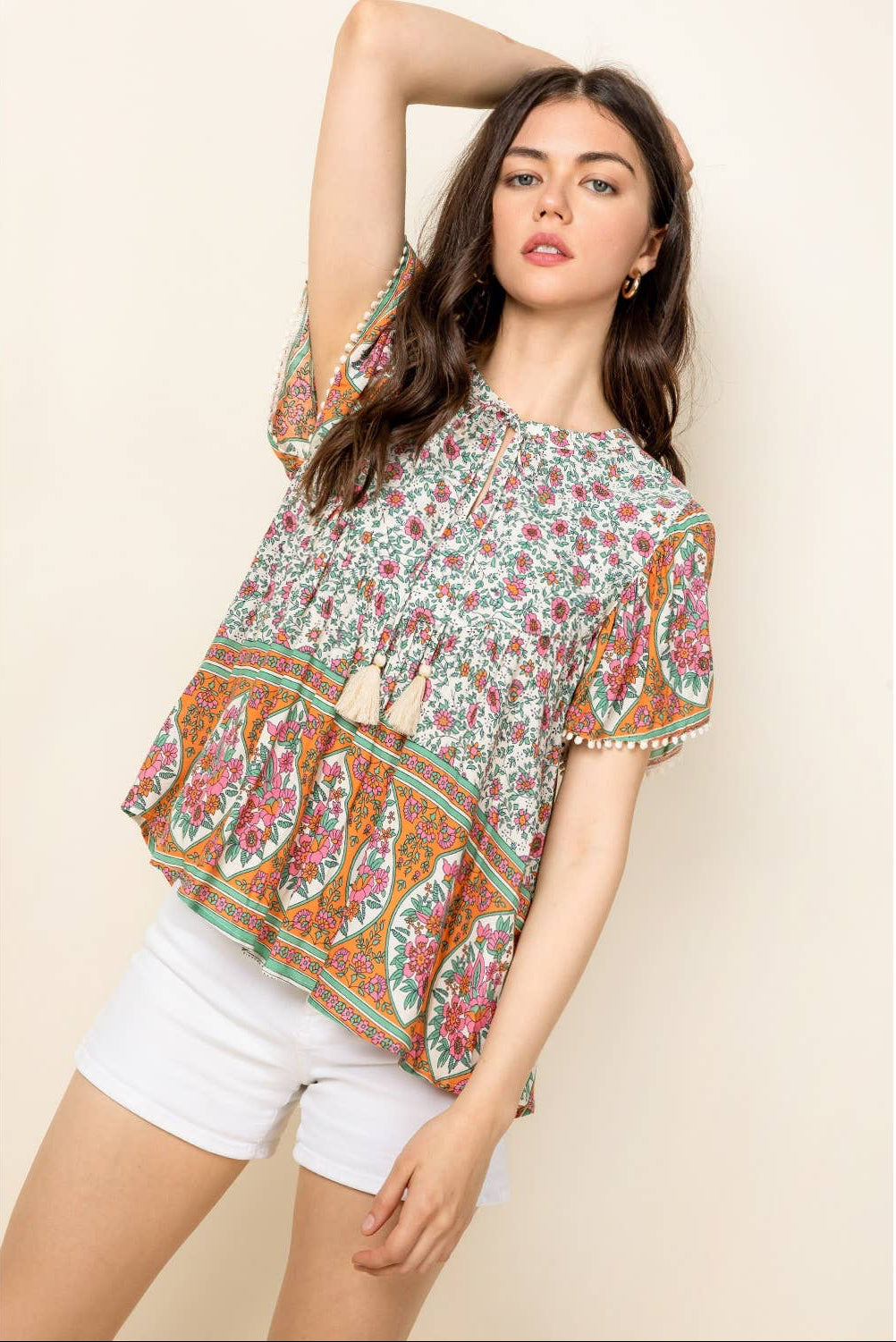 Woman wearing a floral blouse and white shorts on a beige background