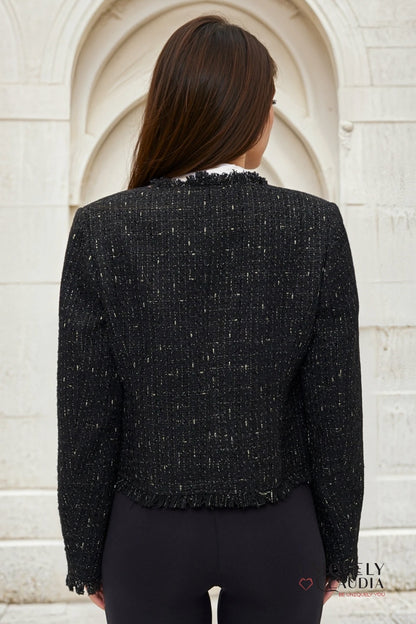 Person wearing a black textured jacket standing against a light-colored wall.
