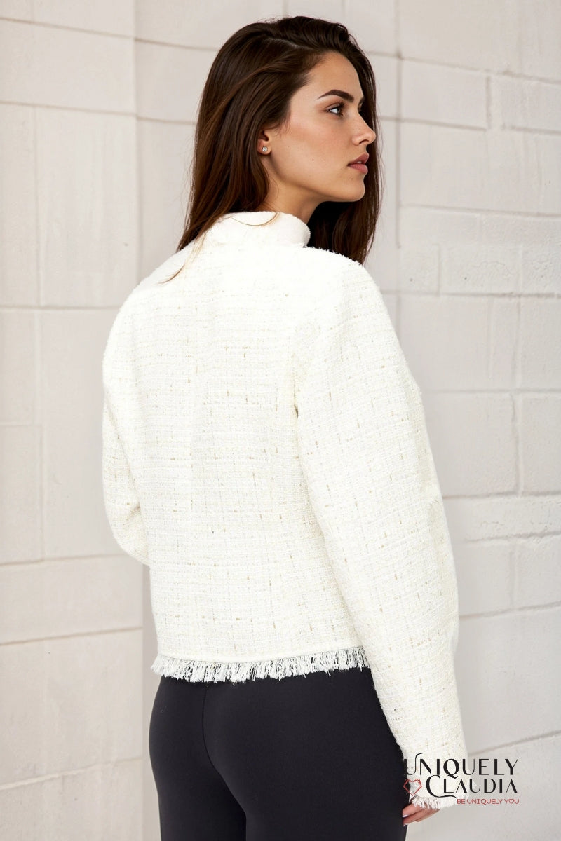Woman wearing a white textured sweater against a light brick wall.