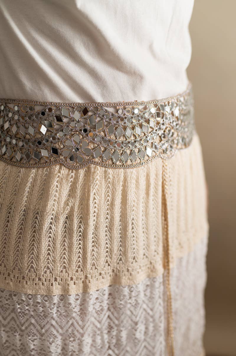 A close-up of a cream and beige embroidered dress or skirt with a wide decorative waistband covered in reflective mirrored tiles.