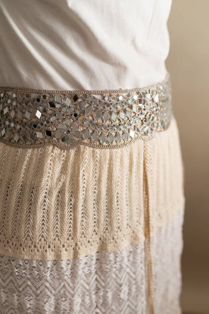A close-up of a cream and beige embroidered dress or skirt with a wide decorative waistband covered in reflective mirrored tiles.