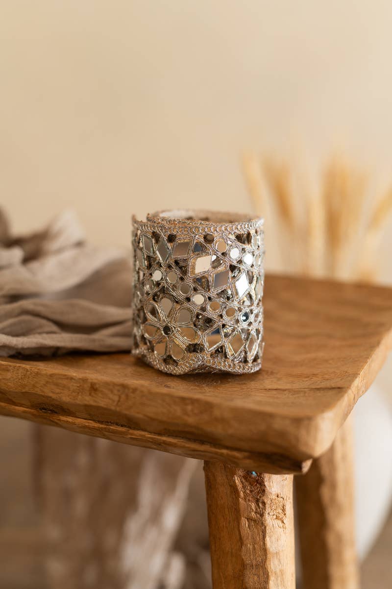 A silver mirrored lace rolled up belt displayed on a rustic wooden table, with a soft beige background and dried grass in the distance.
