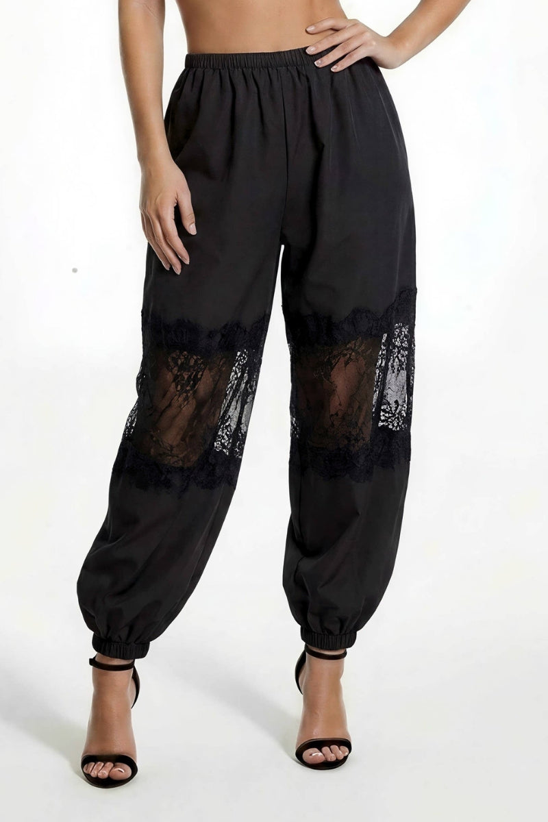 Black harem-style pants with sheer black lace panels on the upper legs, shown on a model wearing black heeled sandals against a plain white studio background.