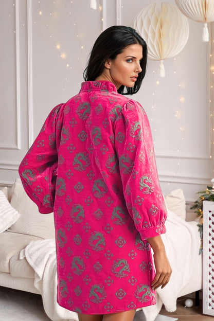 Woman wearing a pink traditional outfit with intricate patterns in a decorated room.