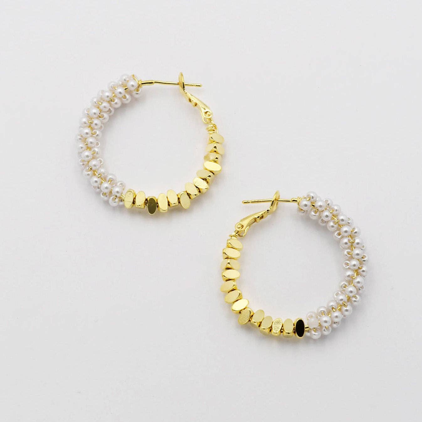 Gold hoop earrings with pearl accents on a light gray background