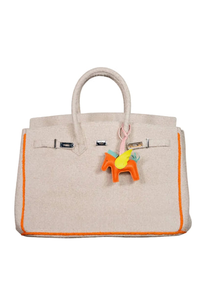 Beige handbag with orange trim and a colorful horse charm on a white background