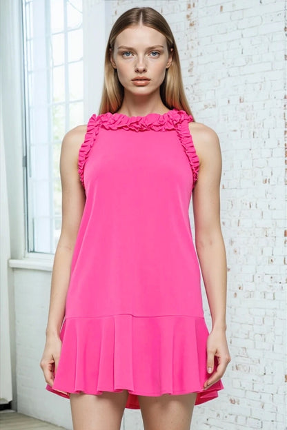 Woman wearing a bright pink dress with ruffled collar against a white brick wall.