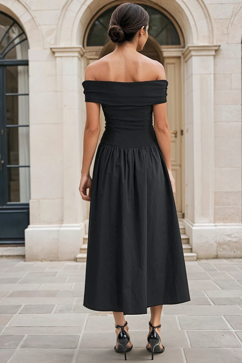 Woman wearing a black off-shoulder dress in front of a stone building.