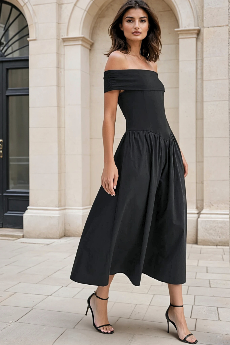 Woman wearing a black off-shoulder dress standing in front of a building.