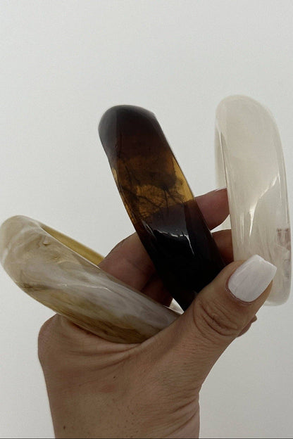 Hand holding three bangles of different colors against a white background